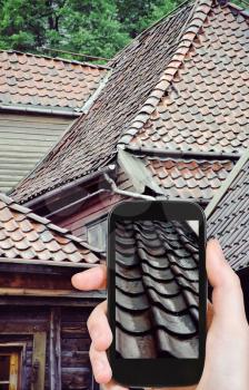 travel concept - tourist taking photo roofs of wooden houses in rain, Bergen, Norway of on mobile gadget