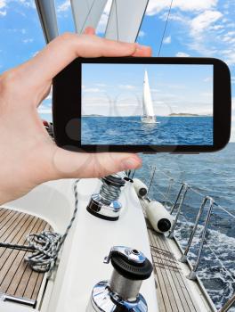 travel concept - tourist taking photo of white sail yacht in blue Adriatic sea, Dalmatia, Croatia on mobile gadget