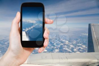 travel concept - tourist taking photo of clouds and lands under wing of airplane on mobile gadget