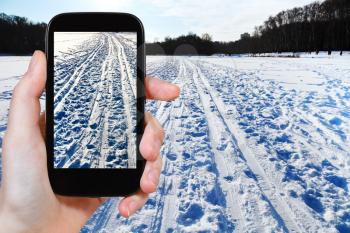 travel concept - tourist takes picture of ski runs in snowy field in cold winter day on smartphone,