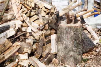 pile of firewoods and several axes in wooden block in village