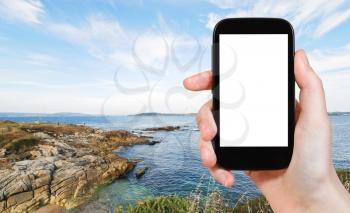 travel concept - tourist photograph coastline of Bay of Biscay in garden of Tower of Hercules near La Coruna town, Galicia, Spain on smartphone with cut out screen with blank place for advertising log