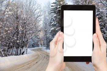 travel concept - tourist photograph country road in snowy russian forest on tablet pc with cut out screen with blank place for advertising logo