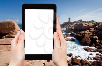 travel concept - tourist photograph lighthouse in rocks on Pink Granite Coast in France on tablet pc with cut out screen with blank place for advertising logo