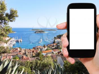 travel concept - tourist photograph town on Hvar island in Adriatic Sea, Dalmatia, Croatia on smartphone with cut out screen with blank place for advertising logo