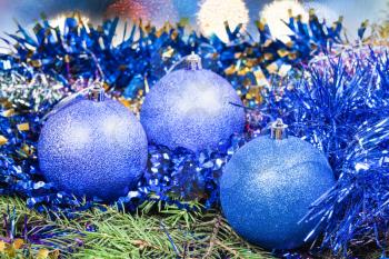 Xmas still life - blue balls, tinsel at green tree with blurred Christmas lights background