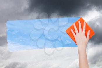 weather concept - hand deletes dark clouds by orange cloth from image and blue sky with white clouds are appearing