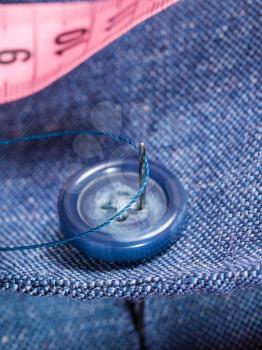 attaching of button to blue silk suit by needle close up
