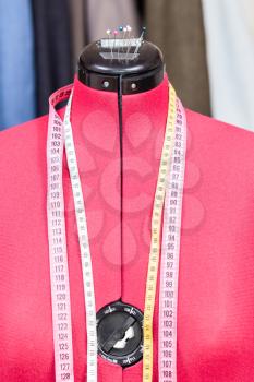 red tailor dummy - mannequin with measure tapes and tissues on background