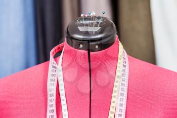 red tailor dummy - mannequin with measure tapes and clothes on background
