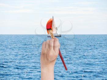 travel concept - hand with paintbrush paints red sail of yacht in blue adriatic sea