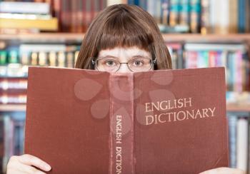girl with spectacles looks over English Dictionary book in library