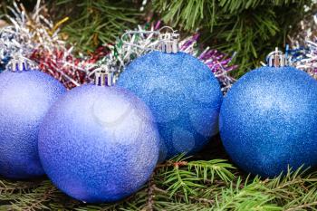 Christmas still life - four blue and violet Christmas balls close up, tinsel on Xmas tree background