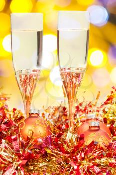 Christmas still life - two glasses of sparkling wine at golden and red Xmas decorations with yellow and violet blurred Christmas lights bokeh background