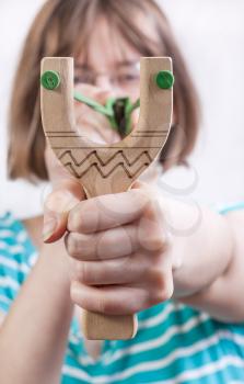 direct view of girl pulling green rubber band of simple wooden slingshot