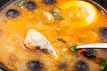 surface of Solyanka russian traditional spicy and sour soup with fish in bowl close up