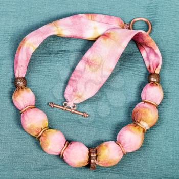 top view of textile necklace from pink and yellow painted silk balls and copper rings on green background
