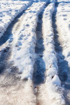 frozen car tracks on snowy country road in cold winter day