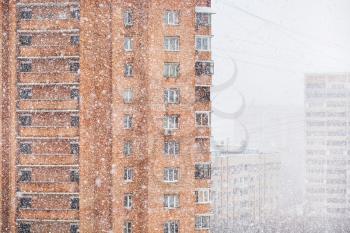 strong snowing and apartment houses in city in winter
