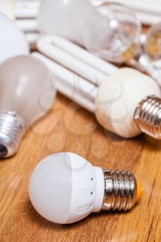 energy saving LED lamp and pile of old incandescent light bulbs and used compact Fluorescent lamps on wooden board