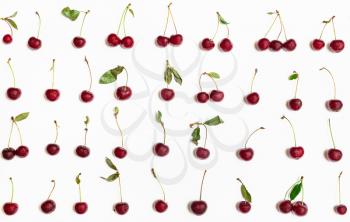 many ripe red cherries with green leaves arranged on white background