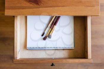 top view of painting brushes on drawing album in open drawer of nightstand