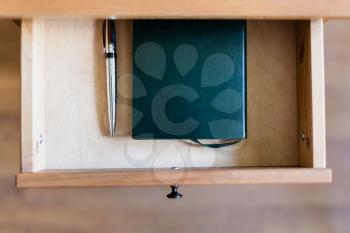 top view of pen and notebook in open drawer of nightstand