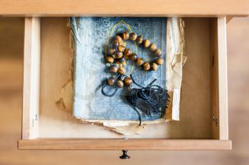 above view of rosary on shabby religious book in open drawer of nightstand
