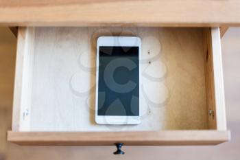 top view of smartphone in open drawer of nightstand