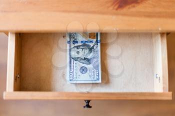 top view of hundred-dollar bills pack in open drawer of nightstand