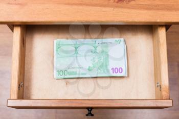 top view of stack of one hundred euro banknotes in open drawer of nightstand