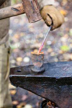 Blacksmith cut out hot metal rod with sledgehammer and chisel on anvil in outdoor rural smithy