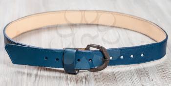 blue leather belt with forged buckle on wooden board