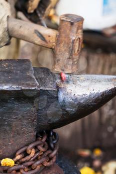 Blacksmith forges sizzling hot metal rod with sledgehammer on anvil in outdoor rural smithy