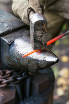 Blacksmith forges red hot steel rod on anvil in outdoor rural smithy