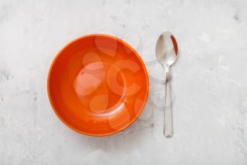 top view of one orange bowl and spoon on gray concrete plate