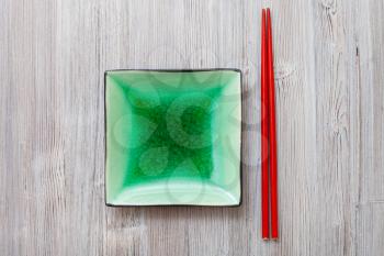 top view of green square saucer and red chopsticks on gray brown table