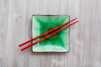 above view of green square saucer with red chopsticks on gray brown board