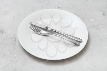 food concept - white plate with parallel knife, spoon on gray concrete surface