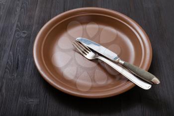 food concept - brown plate with parallel knife, spoon on dark brown table