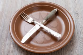 food concept - brown plate with crossing knife, spoon on gray brown table