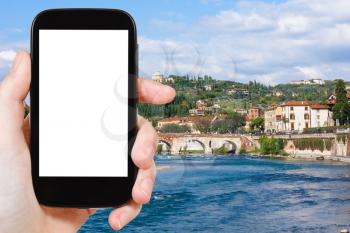 travel concept - tourist photographs Ponte Pietra bridge on Adige river in Verona city on smartphone with cut out screen with blank place for advertising in Italy