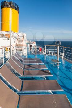 empty sunbathing chairs on upper deck of cruise liner