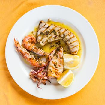 travel to Italy, italian cuisine - top view of sicilian grilled fish and seafood mix on white plate in Sicily