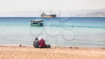 AQABA, JORDAN - FEBRUARY 23, 2012: muslim women on urban beach in sunny winter day. Jordan country has only one exit to sea in Gulf of Aqaba, the length of the coast is 27 km