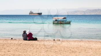AQABA, JORDAN - FEBRUARY 23, 2012: women on urban beach in sunny winter day in Aqaba city. Jordan country has only one exit to sea in Gulf of Aqaba, the length of the coast is 27 km