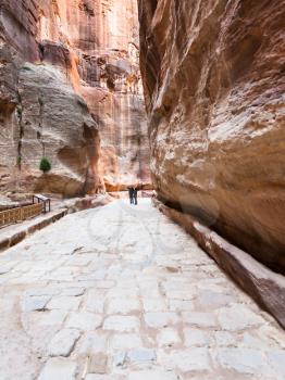 PETRA, JORDAN - FEBRUARY 21, 2012: people on stone paved road in Siq gorge to ancient Petra town in winter. Rock-cut town Petra was established about 312 BC as the capital city of the Arab Nabataean
