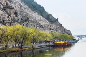 travel to China - view of carved West Hill of Chinese Buddhist monument Longmen Grottoes (Dragon's Gate Grottoes, Longmen Caves) and bridge on Yi river in spring season