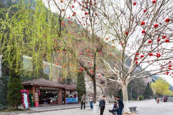 LUOYANG, CHINA - MARCH 20, 2017: tourists near tree with chinese red lanterns on West Hill of Longmen Grottoes (Longmen Shiku, Dragon's Gate Grottoes, Longmen Caves) in spring season