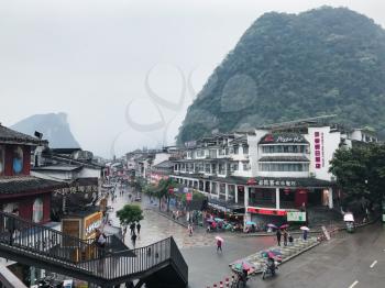 YANGSHUO, CHINA - MARCH 28, 2017: tourists on shopping West Street in Yangshuo city in rainy spring evening. Town is resort destination for domestic and foreign tourists because of scenic karst peaks